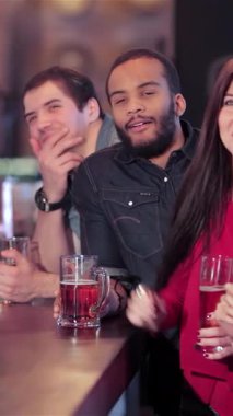 Genç kadın ve erkeklerden oluşan canlı bir grup bardaklarını sevinçle kaldırarak futbol takımlarının zaferini kutluyorlar. Atmosfer heyecan ve kahkahalarla uğulduyor, içkileri ve arkadaşlığı paylaşıyorlar, ruhlarını somutlaştırıyorlar.