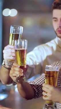 Şık ve şık giyinmiş dört genç adam coşkuyla altın bira kadehlerini kaldırarak coşkulu bir barın coşkulu uğultusuyla çevrelenmiş bir şekilde kadeh kaldırıyor. Bulaşıcı kahkahaları ve tezahüratları havada yankılanıyor.