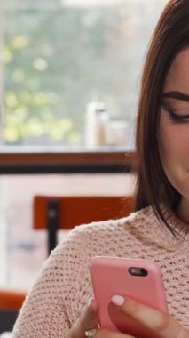 Sıcak, davetkar bir kahve dükkanında akıllı telefonuyla meşgul olan uzun, dalgalı saçları olan neşeli bir genç kadın. Yeni pişmiş hamur işlerinin enfes aroması havada süzülüyor, sıcak atmosferi güçlendiriyor ve onu...