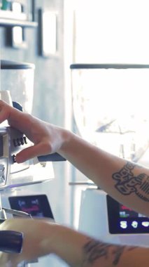 Karmaşık dövmelerle süslenmiş yetenekli bir erkek barista, tutkuyla mükemmel bir espresso yapıyor, odaklanmış bakışları kahve yapma sanatına olan sevgisini yansıtıyor. Etrafı parlak kahve makineleri ve zarif fincanlarla çevrili, canlı kafe atmosferi.