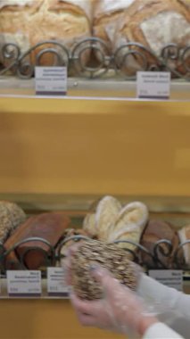 Kafkasyalı genç bir kadın, taze pişmiş bir çavdar ekmeğini canlı bir fırının kırsal ahşap rafına yerleştirirken neşe saçlarıyla dalgalanan kahverengi saçlı bir kadın. Davetkar atmosfer, ağız sulandıran fırın kokusu ile dolu.