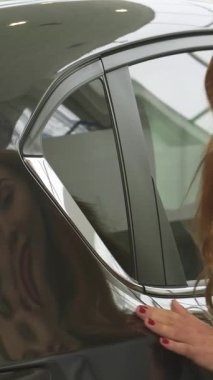 Güzel, kızıl saçlı güzel bir kadının büyüleyici bir yakın çekimi galeride parlak bir arabanın parlak yüzeyine neşeyle dokunuyor. Onun ışıl ışıl gülüşü ve ışıl ışıl gözleri yeni bir araç seçmenin heyecanını yansıtıyor.