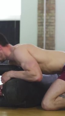 Kendini adamış, kaslı bir adam yoğun bir şekilde eğitim paspası üzerinde bir yan kontrol tatbikatı yapar. Odaklanma ve kararlılık yayar. Spor salonları onun güçlü fiziğine ve karma dövüş sanatlarındaki mükemmelliğine olan sarsılmaz bağlılığına vurgu yapıyor.