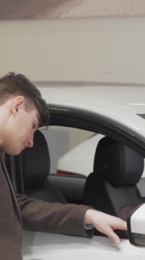 Olgun bir adam, şatafatlı bir galeride lüks bir arabanın içini keşfetmek için merakla eğiliyor. Bu büyüleyici sahne araba alışverişinin heyecanını, modern tasarımı ve potansiyel sahipliğin heyecanını somutlaştırıyor.