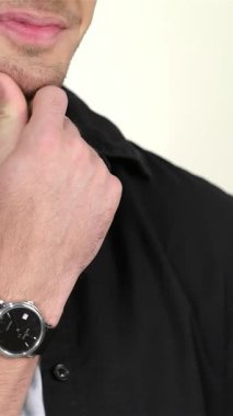 Büyüleyici bir gülümsemesi olan çekici bir genç adam nazikçe çenesini tutarak yumuşak, kremsi bir arka planı olan parlak siyah bir gömleğe güvenir. Şık bir saat ve bakımlı sakalla tamamlanmış düşünceli bakışları davetkar bir yüz yaratıyor.