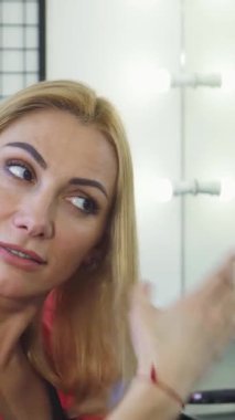 Şık bir kuaförde saçlarını kırık uçlar için endişeyle inceleyen olgun, şık bir kadının yakın çekimi. Parlak, modern ışıklandırma ve zarif dekor, güzellik hizmetinin duygusal ağırlığını yansıtarak saç sağlığı konusundaki endişesini artırıyor.