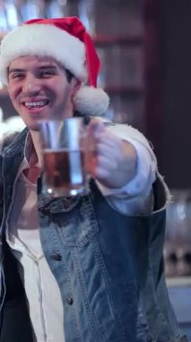 Neşeli bir grup arkadaş, Noel Baba şapkalarıyla süslenmiş, barın önünde kadehlerini neşeyle kaldırıyorlar, sıcaklık ve dostluk saçıyorlar. Barmenlerin neşeli tebessümleri sayesinde hayat dolu atmosfer gelişiyor.