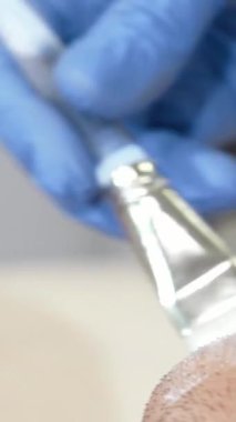 Yakın plan çekimde, yetenekli bir kozmetik uzmanı olarak huzurlu bir mutlulukta olan bir adamın cildini sulandırma ve tazeleme ile saran kremli bir yüz maskesi taktığını görüyoruz. Bu samimi an, kendine bakmanın özünü yansıtıyor, sükunetin ve