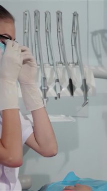 Zarif gözlüklerle süslenmiş gülümseyen bir kadın dişçi ve çıtır çıtır beyaz bir ceket hastalarının ağızlarını dikkatlice inceleyerek profesyonellik ve samimiyet saçıyor. Çekici sarışın hasta dişçi koltuğunda rahatça uzanır, rahatlatıcı bir şekilde sarılır.