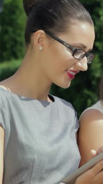 Canlı bir şehir manzarasında, üç güçlü iş kadını dinamik iletişime daldırılıyor, biri telefonla, diğeri ise parlak bir tablet üzerinde işbirliği yapıyor. Şık kıyafetleri ve kararlı ifadeleri güçlü bir atmosfer yayıyor.