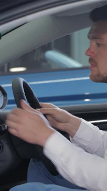 İyi bakımlı sakallı şık bir genç adam, lüks bir arabanın modern ve gösterişli iç mekanını incelemekle yakından ilgilenir. Yüksek teknolojili gösterge paneline odaklanmış bakışları ve dolgun kollukları heyecanını ve merakını yansıtıyor.