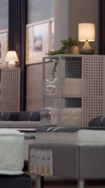 Şık bir adam lüks bir ortopedik yatağın yanında diz çöker ve modern bir mobilya mağazasında konforunu dikkatlice test eder. Zarif dekorlar ve zarif mobilyalarla çevrelenmiş, kaliteli uyku ve sofistike ev yaşamını temsil ediyor.