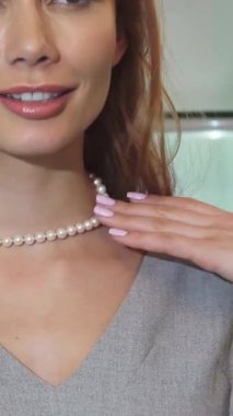 Bu büyüleyici yakın plan, ışıl ışıl gülümseyen, zarif bir mücevher butiğindeki inci kolyeyi zarifçe ayarlayan ışıl ışıl genç bir kadını gösteriyor. Sahne lüks ve kadınsı, izleyicileri moda güzelliğini kucaklamaya davet ediyor.