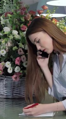 Şık, genç, beyaz bir kadın, parlak cam bir tezgahın üzerine eğiliyor, bir telefon konuşmasına daldırılmış, çarpıcı kırmızı bir kalemle zarif notlar yazarken. Rengarenk çiçeklerin nefes kesici görüntüsüyle çevrili, yaratıcılığını yayıyor ve...