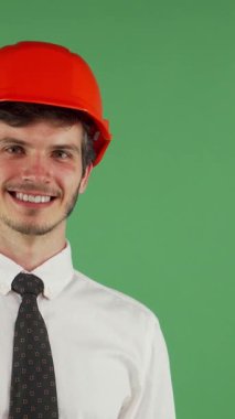 Canlı turuncu bir başlıkla süslenmiş genç, çarpıcı bir erkek mühendis, canlı bir krom arka planda kameraya neşeli bir göz kırpma yapar. Bulaşıcı gülüşü ve kendine güveni inşaat sahasına olan coşkusunu sergiliyor.