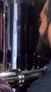 Ekose gömlekli ve önlüklü neşeli bir barmen keyifli bir müşteriyle coşkuyla kadeh tokuşturur, neşe ve dostluk saçar. Parıldayan musluklar ve köpüklü bira ile süslenmiş barlar, canlı bir ortam hazırlıyor.