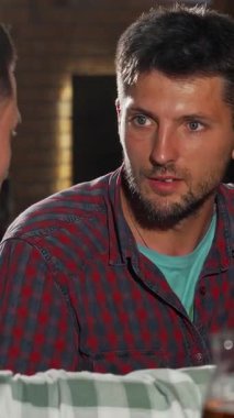 Sıcak, davetkar bir barda, biri genç ve çekici iki erkek arkadaş, diğeri ise daha çok soğuk bira eşliğinde içten bir kahkaha paylaşıyor. Canlandırıcı konuşmaları ve neşeli ifadeleri canlı bir yoldaşlık yayarak bir atmosfer yaratıyor.