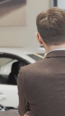 Şık kahverengi takım elbiseli neşeli, olgun bir adam şık bir galeride, göz kamaştırıcı bir modern araç dizisi arasında rüya arabasını tasarlıyor. İfadesi heyecan ve beklenti yayıyor. Seçme heyecanını somutlaştırıyor.