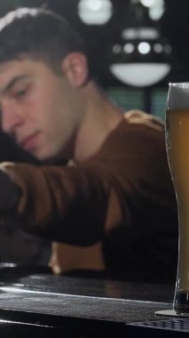 Ön planda pırıl pırıl, altın bir bira bardağı parıldarken, genç bir çift coşkulu bir barın canlı arka planına sevinçle kadeh tokuşturuyor. Bu canlı sahne sevgi ruhunu somutlaştıran sıcaklık ve bağlılık yayar.