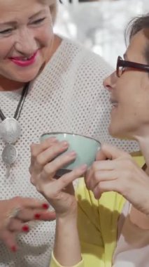 Büyüleyici bir kahve dükkanında, ışıl ışıl yaşlı bir kadın orta yaşlı kızıyla neşeli bir anı paylaşıyor, ikisi de mutluluktan parlıyor. Sıcak gülümsemeleri ve sevgi dolu jestleri aile sevgisinin derin bağını gösteren davetkar bir atmosfer yaratıyor.