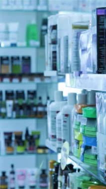 Düşünceli bir ifadeye sahip genç bir kadın yoğun bir eczane koridorunda renkli ürünlerin kaleydoskopuyla çevrili bir şampuan etiketini okumaya dalmış durumda. Bu canlı sahne sağlık ve güzellik alışverişinin heyecanını özetliyor.