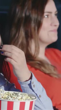 Sıcak bir sinema ortamında, iki genç kadın keyifli bir film gecesinde patlamış mısır yiyip, taze gazoz yudumlayarak eğlenirler. Işıl ışıl gülümsemeleri ve hareketli ifadeleri filmin heyecanını yakalayıp, davetkar bir atmosfer yaratıyor.