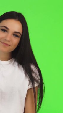 Neşeli, genç, esmer bir kadın pozitiflik saçıyor, canlı yeşil bir zemin üzerinde neşe içinde barış işareti gösteriyor. Büyüleyici gülüşü ve enerjik enerjisi arkadaşlığın ve mutluluğun özünü somutlaştıran sıcaklığı ve bağlantıyı davet ediyor.