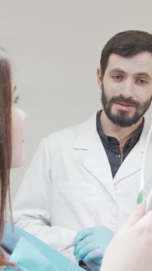 Modern bir diş kliniğinde, kendini işine adamış bir erkek dişçi başarılı bir tedaviden sonra aynada büyüleyici gülümsemesine hayran kalarak mutluluk saçan hastasıyla özenle etkileşime girer. Bu canlandırıcı sahne uyumu güzel bir şekilde gösteriyor.