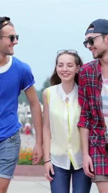 Üç şık genç arkadaş canlı bir şehir caddesinde birlikte yürürler, kahkahaları ılık gün ışığında yankılanır. Bu canlı sahne kaygısız yaz günlerinin özünü yakalıyor, modaya uygun kıyafetlerini ve neşeli atmosferlerini gösteriyor.