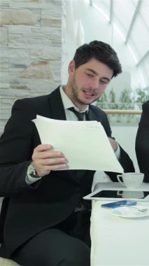 Keskin takım elbiseli odaklanmış genç bir adam, canlı bir ofis ortamındaki işbirliği ruhunu somutlaştıran önemli belgeleri inceliyor. Doğal ışıkla vurgulanan parlak, havadar atmosfer, meslektaşlar arasında yaratıcılığı ve takım çalışmasını teşvik eder.