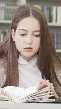 Uzun kahverengi saçlı ve ciddi bir ifadeye sahip kararlı bir genç kız, renkli raflarla dolu canlı bir kütüphanede kitap okurken dizüstü bilgisayarında daktilo yazmakla derinden meşgul. Bu büyüleyici sahne çok güzel.