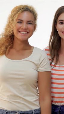 İki hayat dolu genç kadın, biri kıvırcık sarı saçlı ve diğeri parlak kahverengi saçlı, yan yana duran, parlak beyaz bir zemin üzerinde neşeyle parlayan. Hevesli davranışları güven ve dostluk yayıyor, özetliyor.