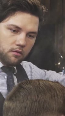 Odaklanmış, yakışıklı, sakallı bir berber erkek müşterilerinin saçlarına sanatsal bir şekilde su püskürtür. Bu da hoş, kaliteli bir berber dükkanındaki stil sürecini güçlendirir. Bu samimi sahne, titiz bir şekilde tımar edilmenin sanatını yakalar.