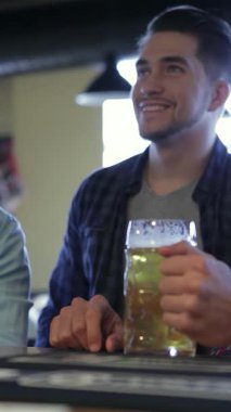 Bir futbol maçının tadını çıkaran üç coşkulu genç adam, hareketli bir barda coşkulu bir kadeh kaldırarak buzlu bardaklarını kaldırıyor. Hayat dolu atmosfer kahkaha ve arkadaşlıkla dolu, dostluğun özünü ve neşesini yakalıyor.