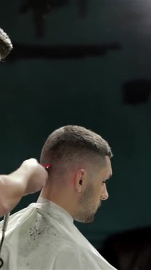 Şık bir berber dükkanında, yetenekli bir berber, sanatını sergilemek için, genç bir adamın saç kesiminde moda bir saç kesimi yapmak için makas kullanır. Titreşimli atmosfer retro dekor ve yumuşak ışıklandırmayla güçlenerek modern tımar için davet edici bir alan yaratıyor.