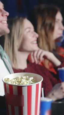 Büyüleyici bir sahne, sinematik sihrin tadını çıkarırlarken yüzleri neşeyle parlayan yedi kişilik bir grup arkadaşı gösteriyor. Patlamış mısırın taşması ve renkli içeceklerle, bu canlı toplantı mutluluk yayıyor,