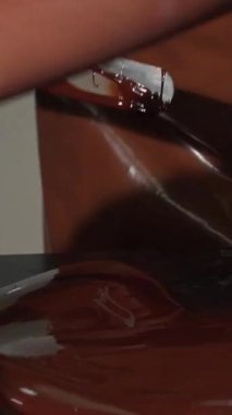 Canlı bir mutfakta, parlak bir önlük ve eldiven giymiş kendini adamış bir çikolatacı, parlak bir tezgahın üzerinde ustalıkla, pürüzsüz, lezzetli bir çikolata yiyor. Bu dinamik sahne, sanatın ve tutkunun ihtişamını gözler önüne seriyor.