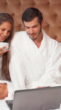 Lüks beyaz bornozlara sarılı mutlu bir çift, keyifli bir sabahı yatakta, dumanı tüten kahveyi yudumlayarak ve dizüstü bilgisayarlarında dijital diyarı keşfederek geçiriyorlar. Gülüşleri zarif bir şekilde tasarlanmış otel odasında yankılanıyor.