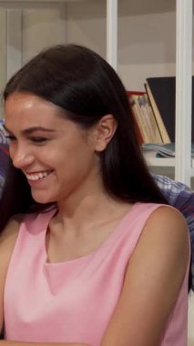 Pembe bluzlu neşeli bir genç kadın ve sıradan giyinmiş erkek sınıf arkadaşı, bir dizüstü bilgisayar üzerinde çalışırken canlı odaklı bir grup akranın arasında parlak bir gülümseme paylaşıyorlar. Bu dinamik sahne takım çalışmasının ve akademik arkadaşlığın ruhunu özetliyor.