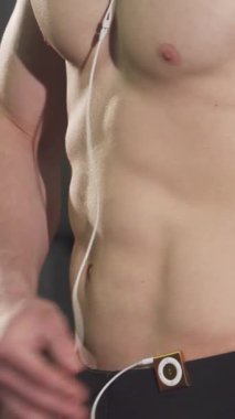 Gömleksiz, kaslı, kaslı, kaslı, kaslı ve kaslı bir adamın antremanına daldırılmış bir halteri kaldırırken, kulaklıkları yerinde. Bu güçlü görüntü azim ve güç yayıyor, sporcuları gösteriyor.