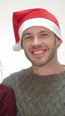 Neşeli bir çift, Noel Baba şapkaları ve rahat kazaklarla süslenmiş, yeni dairelerinin anahtarlarını parlak beyaz bir zemine karşı gururla sergiliyorlar. Işıldayan gülümsemeleri ve sıcacık kucaklaşmaları yeni başlangıçların, aşkın ve tatil ruhunun neşesini yayıyor.