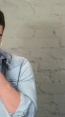 Açık renk kot gömlekli şık bir genç adam aynanın önünde şakacı bir şekilde poz veriyor, büyüleyici bir gülümseme ve yanağında tıraş köpüğü var. Gri tuğlalı bir zemine yaslanmış, özgüven ve modern yetenek yayıyor, davetkar.