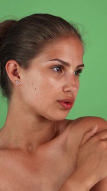 Göz kamaştırıcı, güneş yanığı bir ten rengine sahip genç bir kadın zarif poz veriyor, çıplak omuzları canlı yeşil bir arka plana karşı doğal güzelliğini vurguluyor. Kendine güveni ve yumuşak gülüşü şehvet ve zarafet saçıyor.