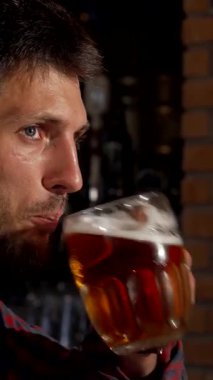 Bakımlı sakalı ve çarpıcı mavi gözleri olan olgun bir adam, buzlu bir bira bardağını kaldırıyor ve kırsal tuğla duvarlarla süslenmiş sıcak, davetkar bir barda neşe saçıyor. Kahkaha ve yoldaşlıkla dolu canlı atmosfer,