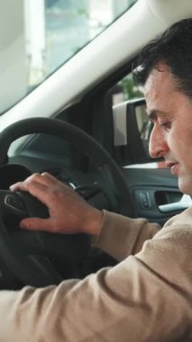 Arka koltuktan bakıldığında, koyu renk saçlı kendine güvenen bir adam arabalara hevesle yaklaşarak dikiz aynasını ayarlıyor ve düğmelere basıyor. Sıcak gülüşü heyecan saçıyor, heyecanını mükemmel bir şekilde yakalıyor.