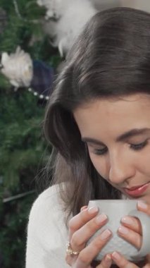 Neşeli bir kadın nazikçe bir fincan buharı tüten çayı kucaklıyor, dingin gülümsemesi göz kamaştırıcı bir şekilde süslenmiş bir Noel ağacının zemininde parlıyor. Bu büyüleyici sahne, izleyicileri aşkın sıcacık sıcaklığında güneşlenmeye davet ediyor.