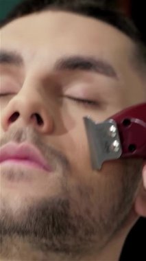 Canlı bir berber dükkanında, yetenekli bir berber rahat bir erkek müşterinin üzerinde ustalıkla şık bir sakal kesiyor ve yontuyor, tımar sanatını sergiliyor. Kaliteli dekor ve hassasiyet araçlarıyla vurgulanan ılık ortam, davetkar bir davet yaratıyor.