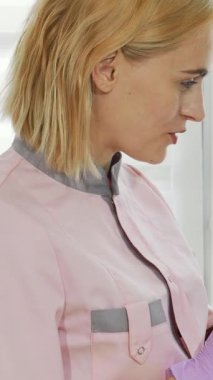 Kendini işine adamış pembe üniformalı ve mor eldivenli bir kozmetik uzmanı, yumuşak beyaz bir bornozla rahatça örtünen olgun bayan müşterisiyle sıcak bir ilişki içindedir. Huzurlu atmosfer, yaklaşan olayları tartışırken özen ve profesyonellik yayıyor.