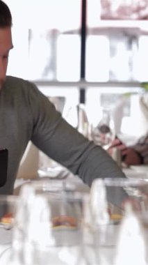 Şık bir kafede, rahat giyimli genç bir işadamı tabletine odaklanmış lezzetli bir yemeğin tadını çıkarıyor. Zarif masa ayarları ve yumuşak ışıklandırmayla vurgulanan şık ortam, üretkenlik ve gevşemenin uyumlu bir karışımını yaratır.