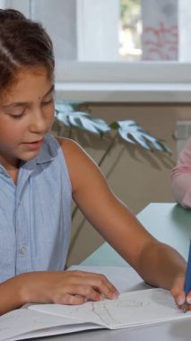 Kendini saçlarını dalgalandırmaya adamış küçük bir kız, arka planda gururla ışıldayan destekleyici öğretmeni gibi elinde kalemle çizimine yoğun bir şekilde odaklanmış durumda. Bu canlandırıcı sahne yaratıcılığı ve teşvikleri parlak bir sınıfta yayıyor.